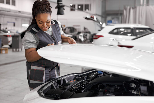 black female is opening the hood of white car in auto repair shop, want to check the oil level in car engine, side view. female auto mechanic checking and maintenance car engine or vehicle