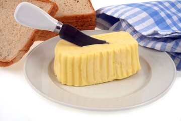 Beurre dans une assiette avec un couteau planté dedans à côté de tranches de pain de mie sur fond blanc