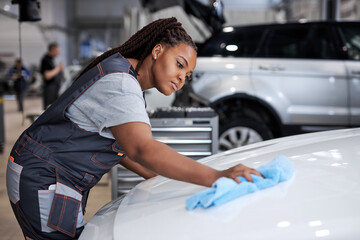 Beautiful african woman holds blue microfiber in hand and polishes the car. Cleaning washing auto....