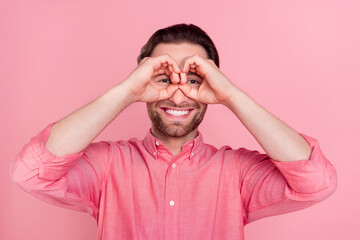 Photo of positive funky funny young man hold hands fingers make glasses ok sing isolated on pink color background