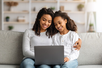 Happy african american mother and daughter using laptop together
