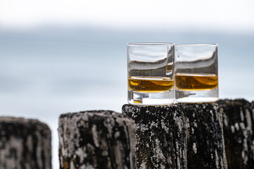 Tasting of dram single malt scotch whisky on seashore in Scotland, old wooden pole with whisky glass
