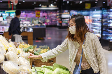 Asian woman wearing protect face mask and  shopping fruit, vegetable in grocery department store.