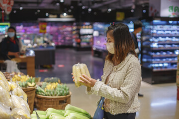 Asian woman wearing protect face mask and  shopping fruit, vegetable in grocery department store.