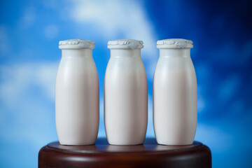 Natural liquid yogurt with probiotics in small plastic bottles on wooden table on background of blue sky with clouds. Healthy, balanced diet food, healthy breakfast, dairy products.
