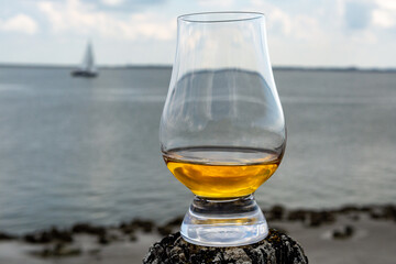 Tasting of dram single malt scotch whisky on seashore in Scotland, old wooden pole with whisky glass