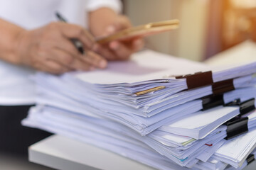 Paperwork files searching information business concept, Businessman hands using smartphone for working in stacks of report papers and piles of unfinished documents achieves on office desk