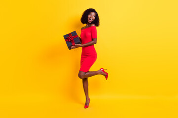 Full size photo of young excited positive afro girl look copyspace hold birthday present isolated on yellow color background