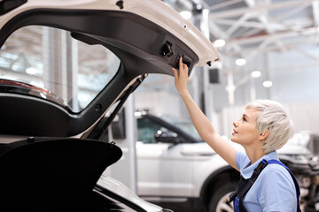 Short Haired Caucasian Female Auto Mechanic Is Opening Car Trunk, Side View, Young Woman In Overalls Uniform Is Going To Clean Or Repair White Automobile. Copy Space