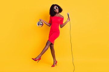 Full length body size view of pretty cheerful girl singing hit holding disco ball isolated over bright yellow color background