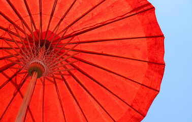Under side of red handmade paper umbrella with blue sky background. 