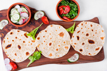Three tortilla flatbreads and sliced vegetables on the wooden board. Cooking Mexican food, taco or fajitas