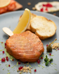Close up of Unusual fish dish on stick. Exotic appetizer wrapped in slice of fish, garnished with red caviar, lemon, croutons and capers on gray plate. Soft focus. Vertical format.