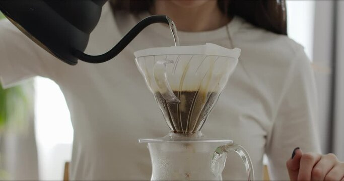 Process of brewing pour over coffee with V60 decanter. Barista girl spilling ground grains with water in a paper filter. Professional set for making a pourover at home