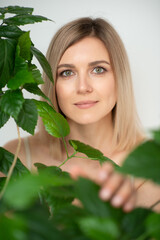 Fototapeta premium Beautiful calm middle aged woman with green plant, natural light. Anti-aging and beauty treatment.
