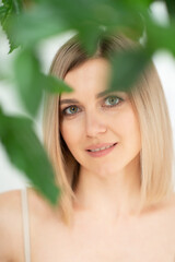Fototapeta premium Beautiful calm middle aged woman with green plant, natural light. Anti-aging and beauty treatment.
