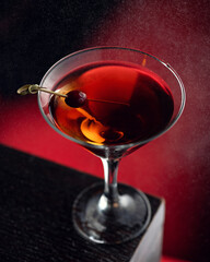 Strong alcoholic cocktail or drink with cherry, backlit on dark red background surrounded by fine water spray. Vertical format, soft focus.