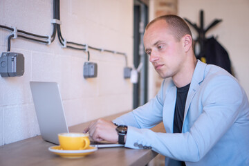 Young successful businessman sitting at coffee in a cafe and working on his laptop.