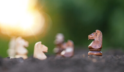 Wooden horse in chess game face with the another yellow team on soil with green blur bokeh background. Shot of a chess board brown horse moving with shallow depth of field. Soft focus