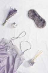 Sleep mask, silk pajamas, aroma balsam, dry lavender flowers on white bedclothes. Concept healthy dream.