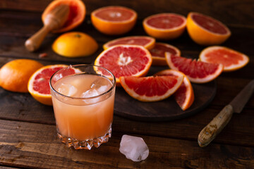 sliced pieces of grapefruit lie on the table on the dark wooden countertop. next to it is a glass of freshly squeezed grapefruit juice