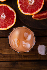 sliced pieces of grapefruit lie on the table on the dark wooden countertop. next to it is a glass of freshly squeezed grapefruit juice