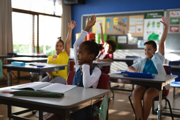 Group of diverse students raising their hands in the class at elementary school