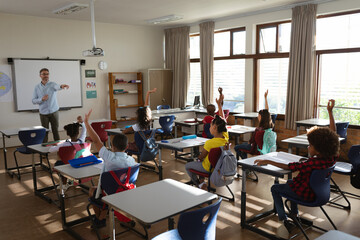 Group of diverse students raising their hands in the class at elementary school