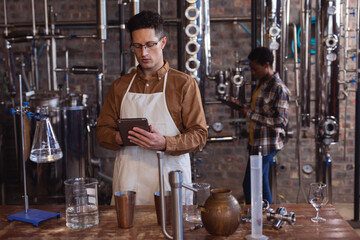 Caucasian male worker wearing apron using digital tablet at gin distillery