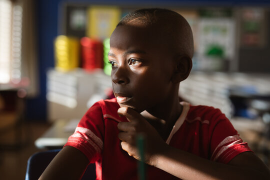African american boy looking out of window while siting on his desk in class at elementary school