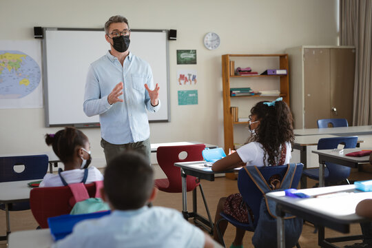 Caucasian male teacher wearing face mask teaching in the class at elementary school
