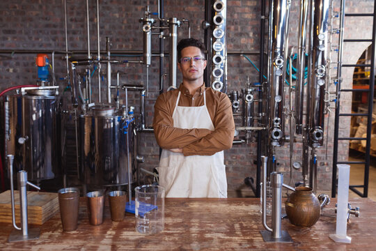 Portrait of caucasian male worker wearing apron standing with arms crossed at gin distillery - Powered by Adobe