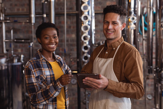 Portrait of diverse male and female worker with digital tablet smiling at gin distillery