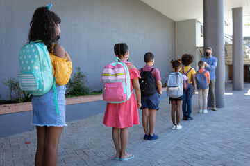 Caucasian male teacher measuring temperature of group of students standing in a queue at school
