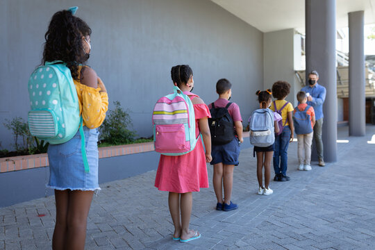 Caucasian male teacher measuring temperature of group of students standing in a queue at school