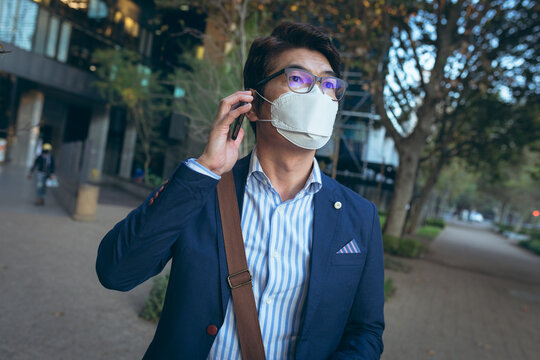 Asian businessman wearing face mask using smartphone in city street