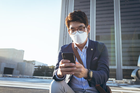 Asian businessman wearing face mask using smartphone in city street