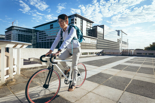 Asian businessman riding bike in city street with modern buildings in background