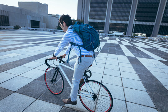 Asian businessman riding bike in city street with modern buildings in background