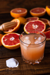 sliced pieces of grapefruit lie on the table on the dark wooden countertop. next to it is a glass of freshly squeezed grapefruit juice