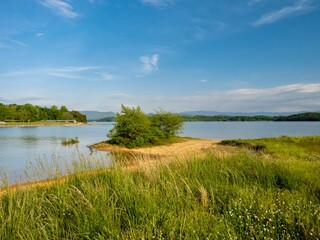 Douglas Lake in the spring in Tennessee with the Great Smoky Mountains in the background, the water and sandy shore with a blue sky filled with clouds in the distance.