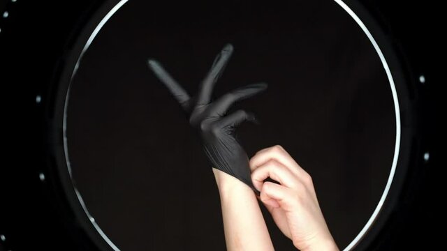 Woman wearing black latex gloves in a beauty salon with beautiful circular lighting. Preparation for the procedure in the salon