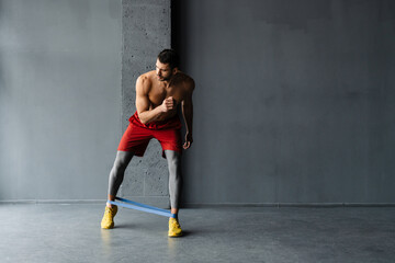 Young shirtless sportsman doing exercise with expander stretch tape