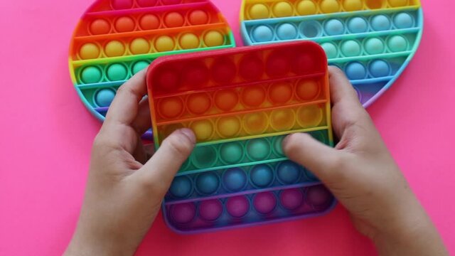 colorful antistress sensory toy fidget push pop it in kid's hands on pink background