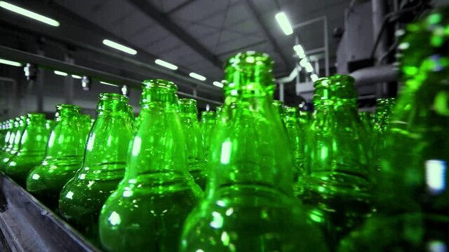 line for filling beer in a brewery. Empty green glass bottles moving on a conveyor belt in a queue at a beer factory.