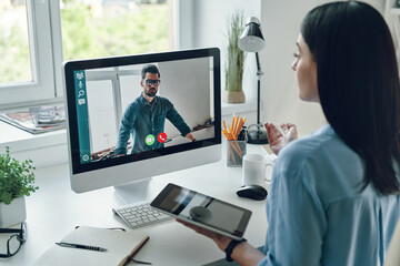 Serious young woman talking to collegue by video call while sitting in office