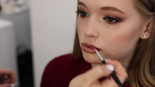 makeup artist paints lips with lipstick with a brush on a beautiful young woman blonde model, face make up concept