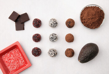 variety of healthy cacao truffle snacks on white tabletop showing ingredients including avocado and sprinkles from above