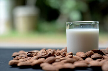 almond milk in a glass with almonds on black table, good for health, front view with selective focus