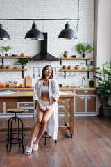 laughing young adult woman in white bathrobe holding cup of coffee in modern loft